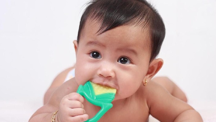 Portrait of cute little Asian baby girl lying down on bed and biting rubber toy