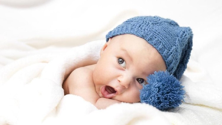 baby boy lying in bed, in blue cap