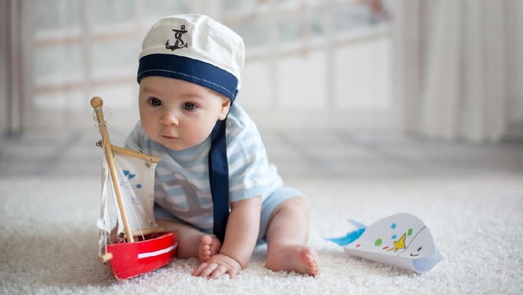 Little baby boy, playing wtih little boat and little fish at home, having sailor hat