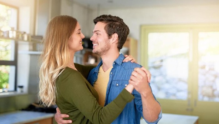 Romantic couple at home. Attractive young woman and handsome man are enjoying spending time together. Sitting on the floor in light modern kitchen.