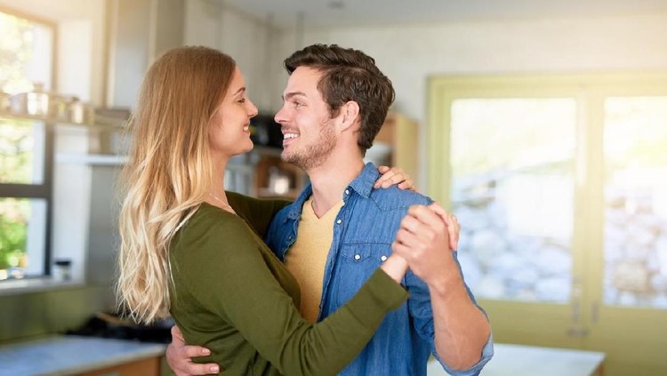 Romantic couple at home. Attractive young woman and handsome man are enjoying spending time together. Sitting on the floor in light modern kitchen.