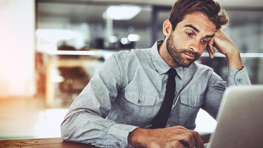 Shot of a handsome young businessman looking bored while working on a laptop in an office