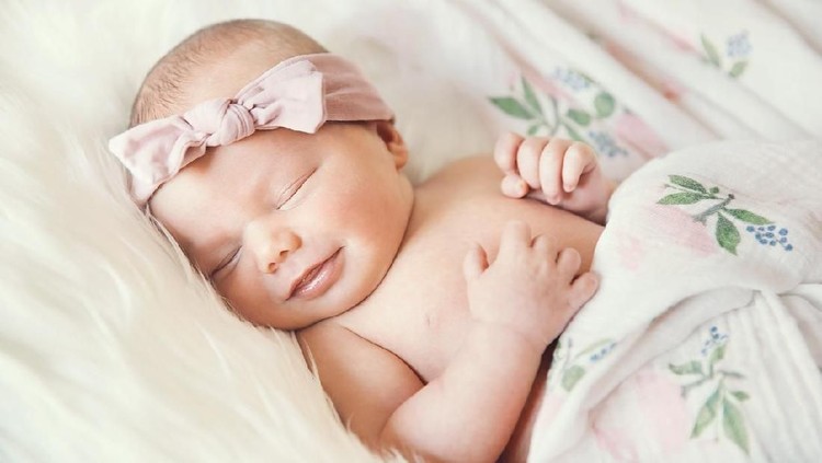 853843646 Sleeping newborn baby in a wrap on white blanket. Beautiful portrait of little child girl 7 days, one week old. Baby smiling in a dream.
