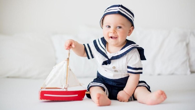 Cute baby boy, dressed in sailor clothes, playing with wooden boat