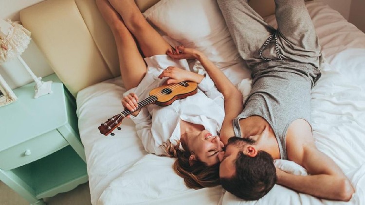 Lovely couple in pyjamas spending morning in their bed, celebrating Valentine's day by playing an ukulele