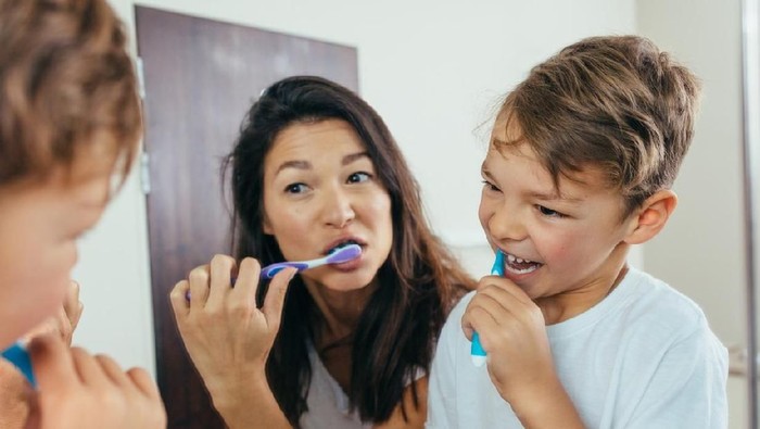 Mother and son brushing teeth in bathroom. Woman with her son brushing teeth together and looking in mirror.