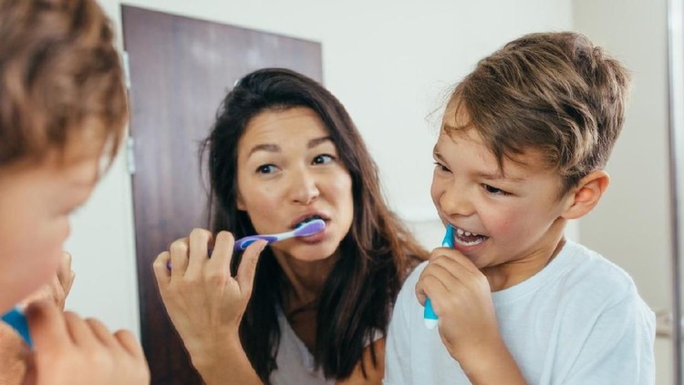 Mother and son brushing teeth in bathroom. Woman with her son brushing teeth together and looking in mirror.