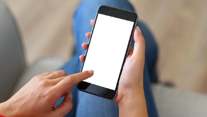 Woman using and touching a blank white screen smart phone on a couch.