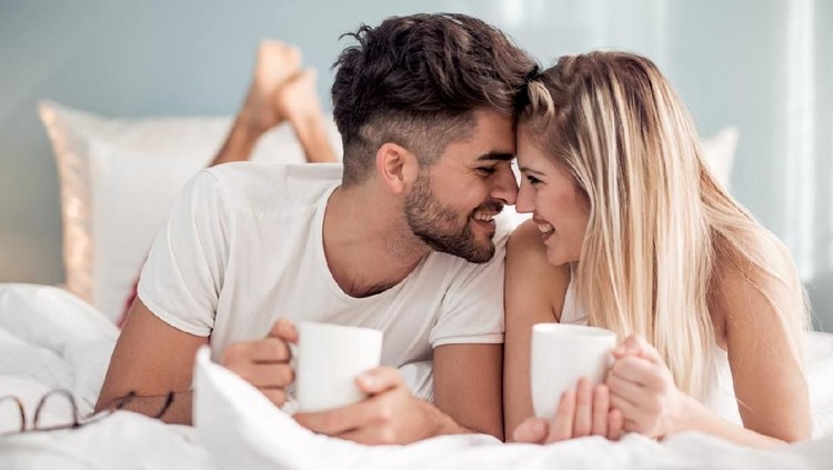 Young beautiful couple drinking coffee in bed at morning.