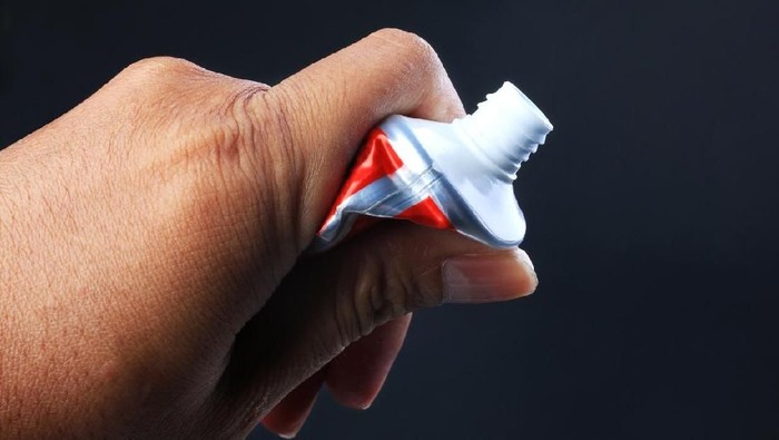 Child's hand squeezes the toothpaste on the toothbrush