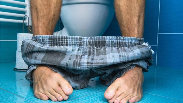 A patient bends over an examining table as a doctor squeezes lubricant onto his finger to do a prostate examination.