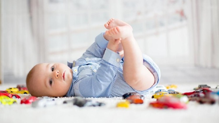 Adorable baby boy, lying on the floor, toy cars around him , looking at the camera, shot from above