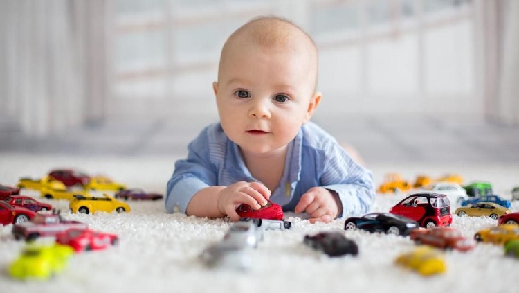 Adorable baby boy, lying on the floor, toy cars around him , looking at the camera, shot from above