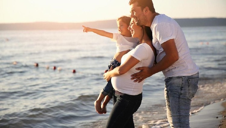 Pregnant woman with child. Mother and son on nature background, close-up. Child boy is sitting on belly of his mother, who pregnant for second time. Pregnancy, new life, family, parenthood concept.