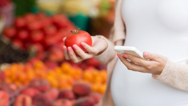 Woman holding red tomato in one hand, and the second with a pregnant belly. Close-up of a pregnant woman on a black background. Concept of healthy diet for the baby
