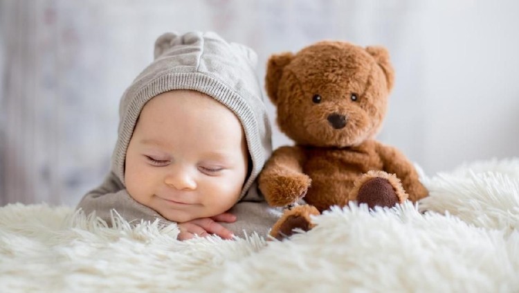 Sweet baby boy in bear overall, sleeping in bed with teddy bear stuffed toys, winter landscape behind him