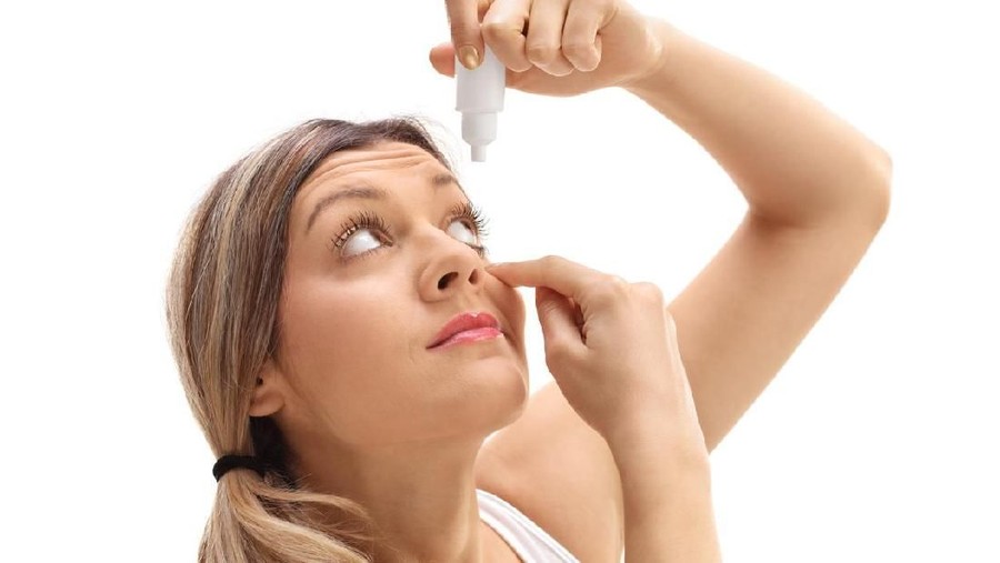 Young woman applying eye drops isolated on white background