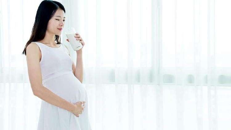 ilustrasi susu hamil Pregnant woman sitting on sofa and drinking milk