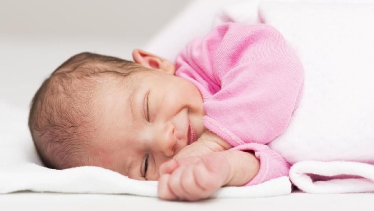 Portrait of a newborn baby girl while sleeping and smiling.