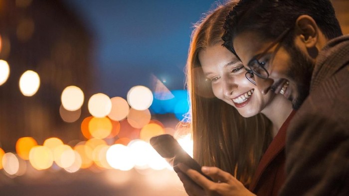 Young couple enjoying time together in London. They are standing, using phone and laughing.