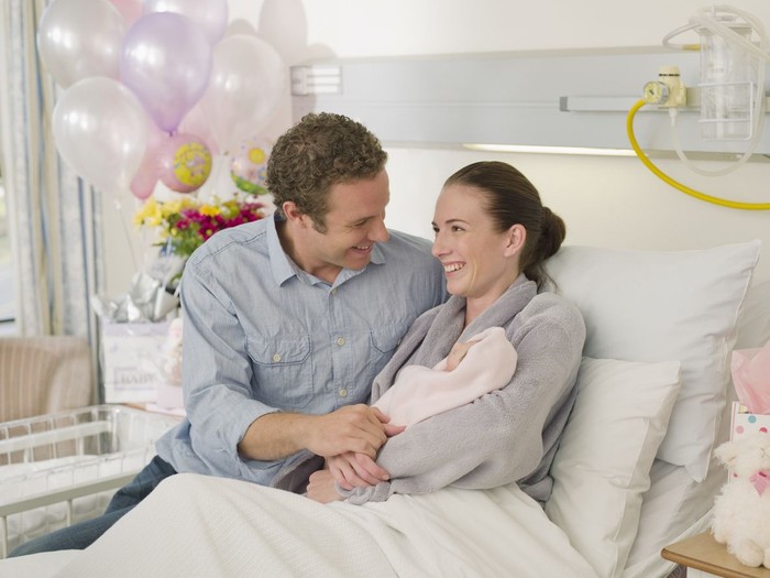 In the Hospital Mother Hold Newborn Baby, Supportive Father Lovingly Hugging Baby and Wife. Happy Family in the Modern Delivery Ward.