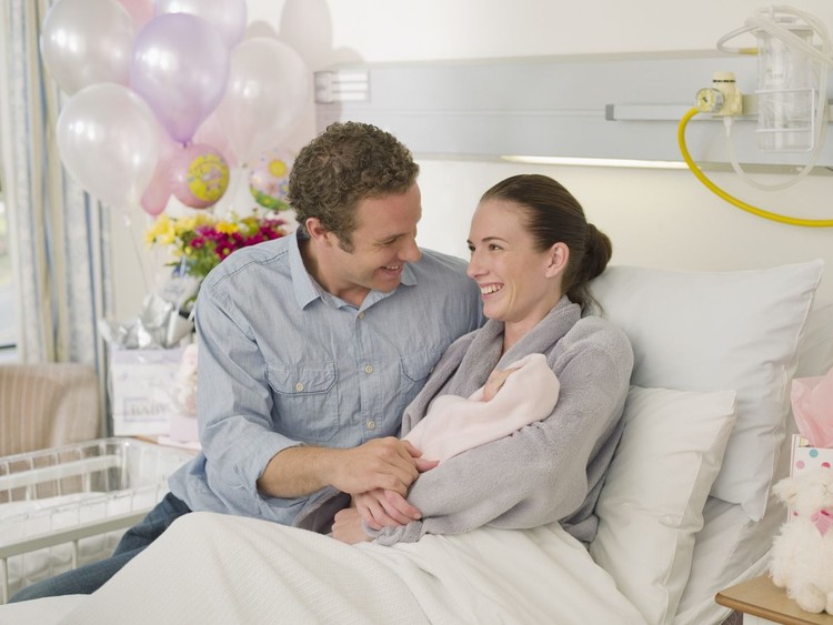 In the Hospital Mother Hold Newborn Baby, Supportive Father Lovingly Hugging Baby and Wife. Happy Family in the Modern Delivery Ward.