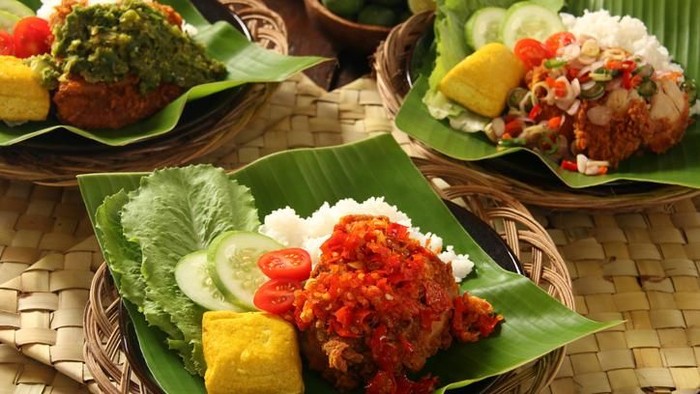 Ayam Geprek, the popular fusion street food dish of southern fried chicken served with traditional spicy condiments from regional cuisines in Indonesia. Here each of the chicken piece is topped with a popular condiment, such as Sambal Lado (lightly red chili paste) and Sambal Lado Mudo (green chili paste), both from West Sumatra, and Sambal Matah (chili pepper, lemon grass and shallot salsa) from Bali. The chicken and condiment are served with steamed rice, yellow tofu, and fresh vegetables. The dish is plated on a ceramic plate lined with banana leaf; which then placed on a woven stick plate.