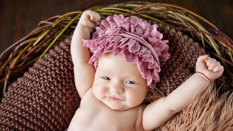 bayi A laughing, crawling, seven month old, baby girl wearing a white shirt, diaper and headband. Shot in the studio on a white, seamless backdrop.