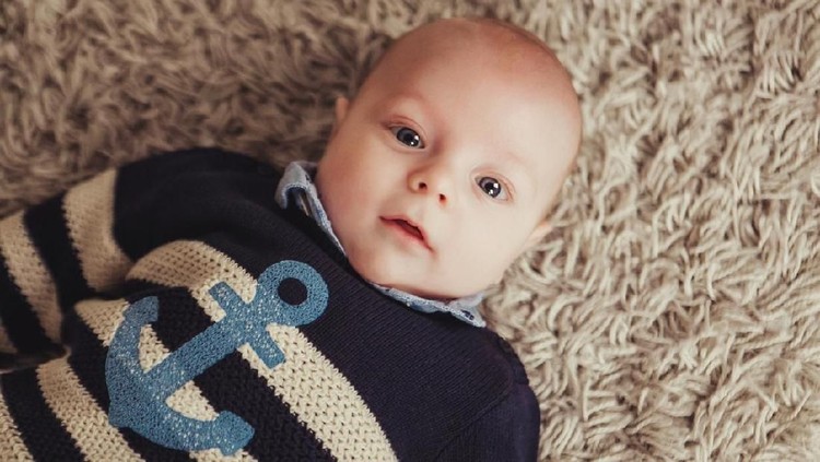 907202770 Cute little baby boy with handmade knitted cloths, playing with little teddy bear toy, smiling at camera