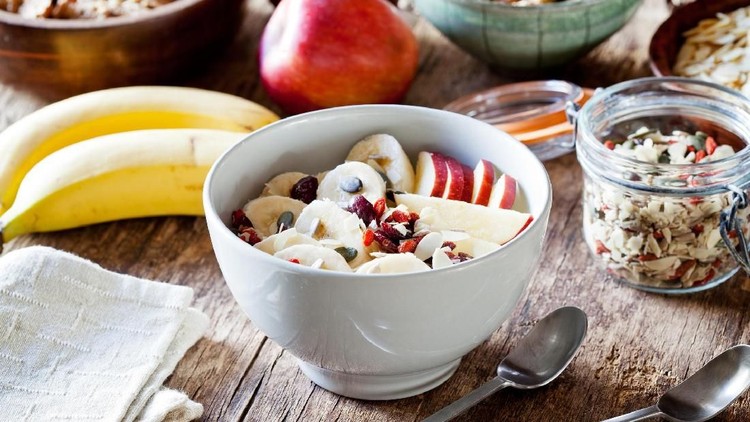 A selection of different Summer fruits, in a variety of bowls on a painted blue wood planked farmhouse kitchen table, against a light blue background.