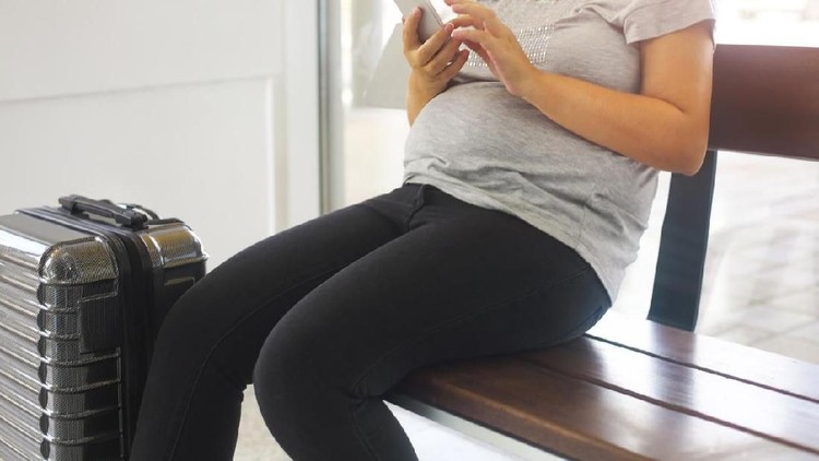 Young pregnant woman with suitcase at airport or station