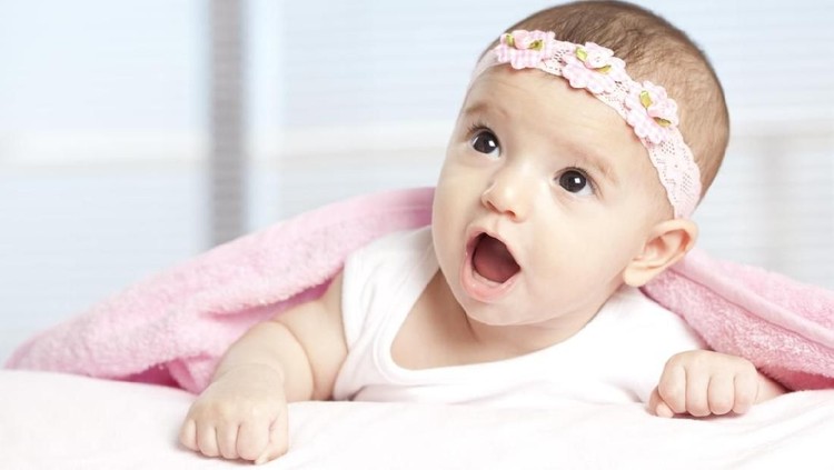 Little baby girl lying on bed,smiling and looking at camera.She got teddy bear hat on head.