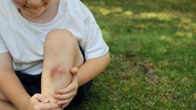 Young boy holds a sore leg that received a injury while playing outdoors.