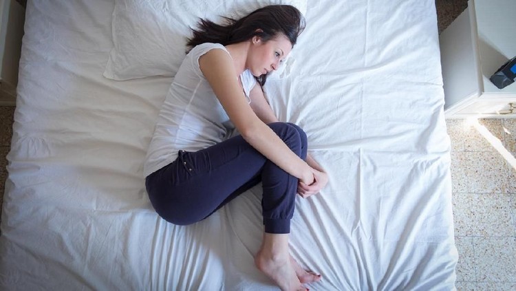Sad lonely woman lying in the bed in fetal position