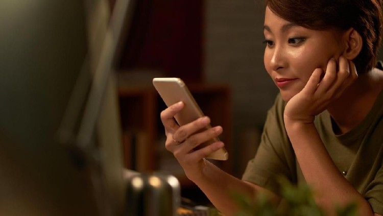 Closeup of thoughtful young Asian woman holding mobile phone and surfing Internet. Attractive student taking selfie at cafe. Communication and work balance concept