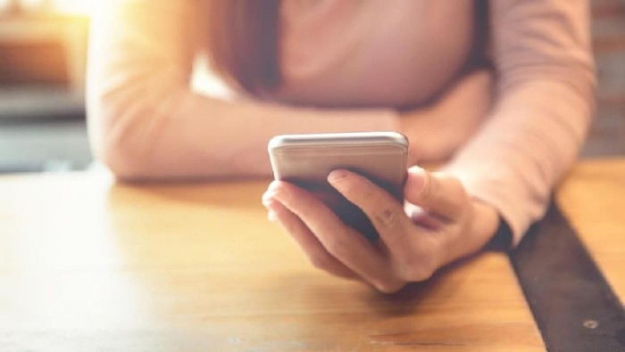 Closeup of thoughtful young Asian woman holding mobile phone and surfing Internet. Attractive student taking selfie at cafe. Communication and work balance concept