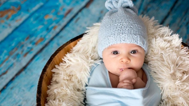 Little baby boy with knitted hat in a basket, happily smiling and looking at camera, isolated studio shot