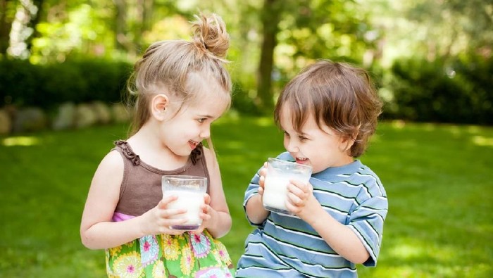 Color image of a little boy and a little girl sitting outside drinking a glass of milk and smiling at each other. Focus is on little boy.