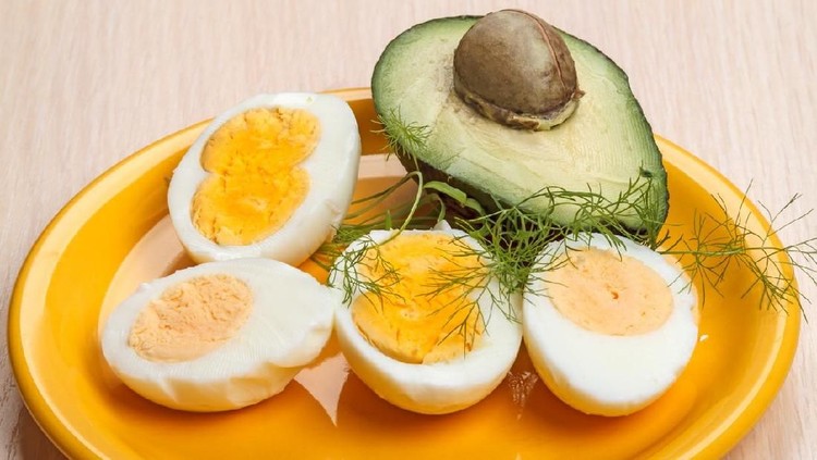 Four halves of boiled eggs and avocado on a yellow plate. Egg with two yolks