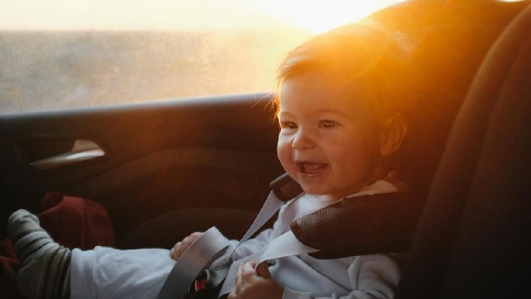 Cute baby boy driving in his car seat with a smile