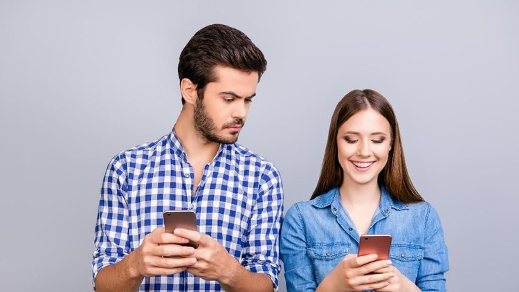 Curious boyfriend is spying his lover`s smartphone. They are wearing casual shirts, standing isolated on pure background