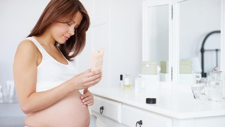bayi tabung A beautiful pregnant woman rubbing skin moisturiser on her baby bump in the bathroom