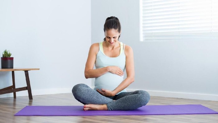 Pregnancy yoga meditation. Full length healthy 8 months pregnant calm Asian woman meditating or doing yoga exercise at home. Relaxation yoga sitting side stretch positions.