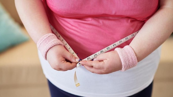 Close-up of overweight woman measuring her waist with tape measure