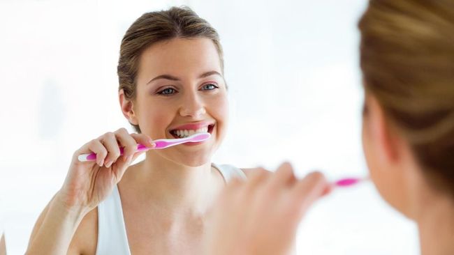 Portrait of pretty young woman brushing her teeth in the bathroom at home.