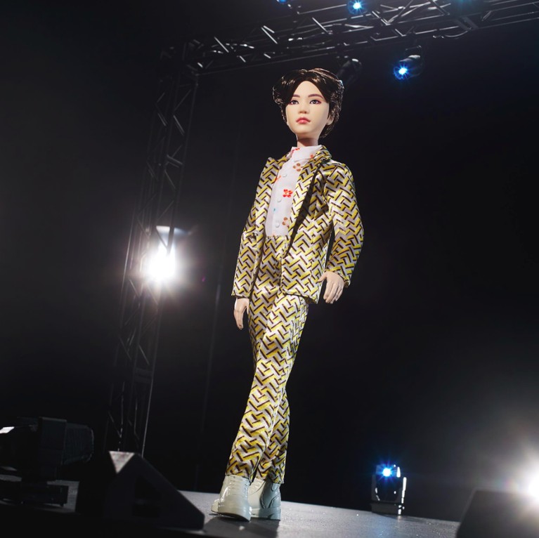 Dalam bentuk action figurenya, Suga BTS dibuat lebih glowing dengan blazer dan celana berwarna emas. Dan di padukan dengan sepatu dan kemeja dalam berwarna putih.