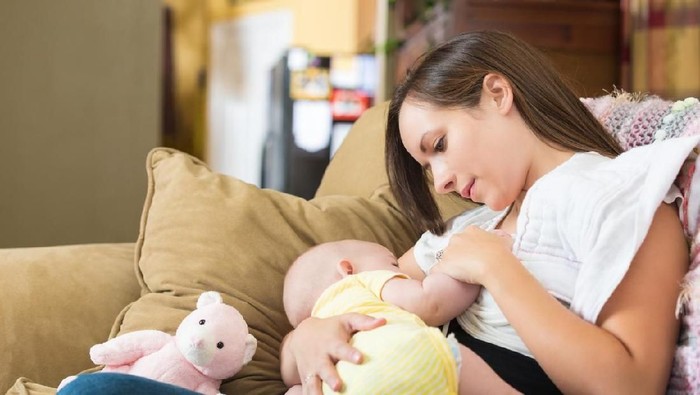 Young mom breastfeeding infant daughter at home