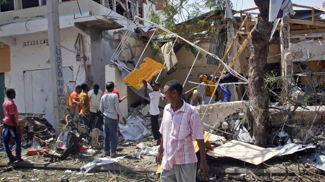 Somalis walk near wreckage at the scene following an attack outside a restaurant in Mogadishu, Somalia Thursday, March 28, 2019.  An explosives-laden vehicle detonated outside a busy restaurant in Somalia's capital, killing at least 10 people, police said Thursday. (AP Photo/Farah Abdi Warsameh)