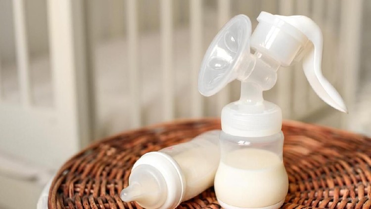 Breast pump and bottle with milk for baby on a straw basket. Kids room with a bed.