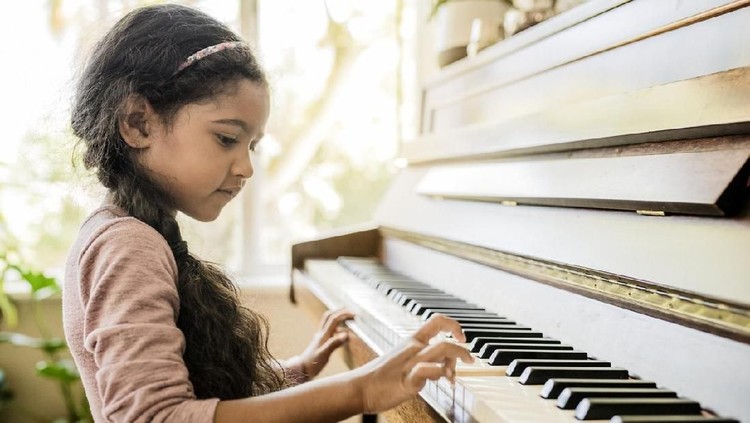 bakat anak Side view of girl playing piano. Cute female child is practicing on musical instrument. She is at home.
